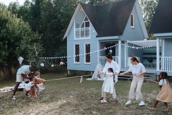 Happy family playing tug of war in front of cozy houses during a summer day.